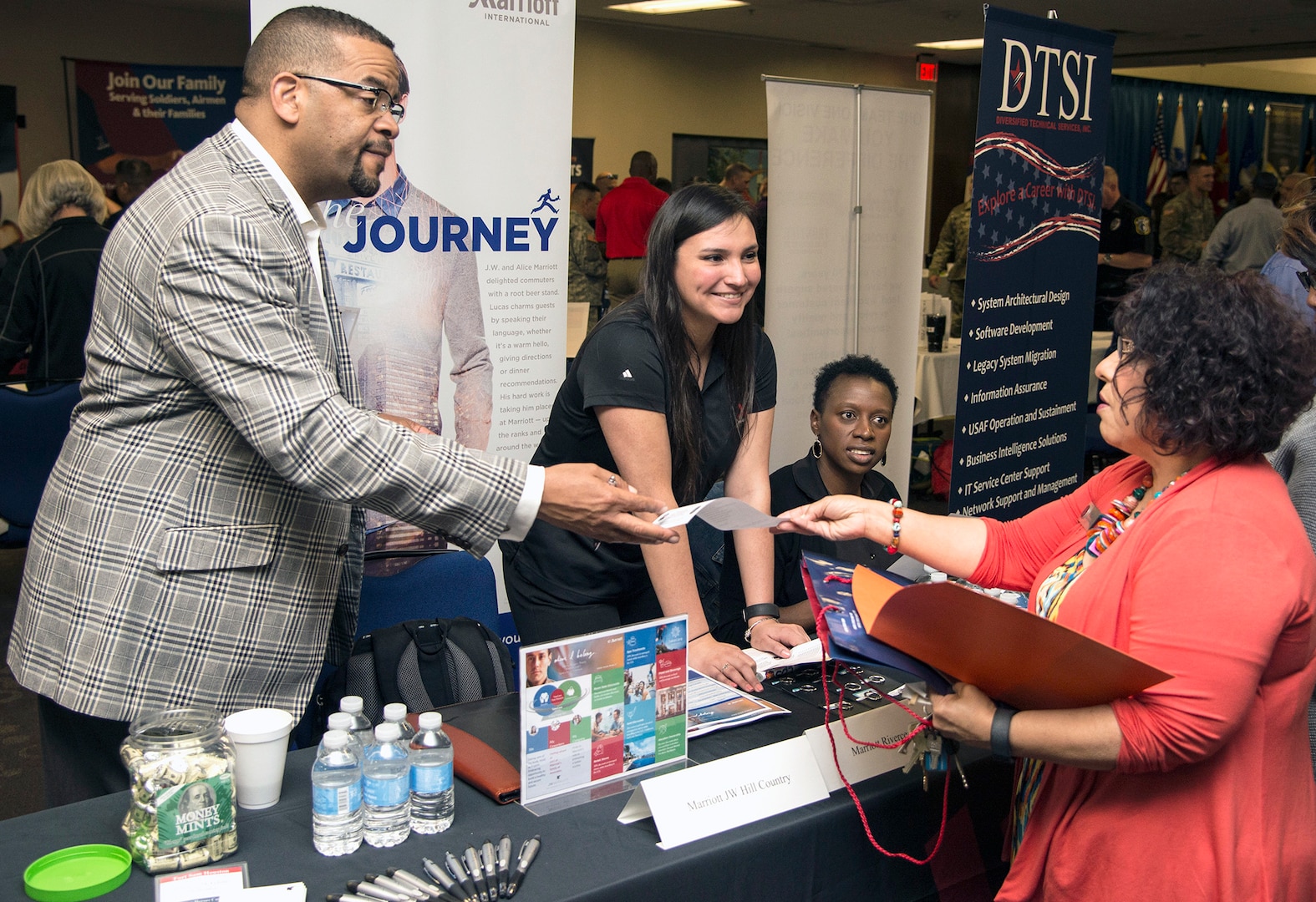 A company recruiter hands information to a visitor on a career opportunity at the Hiring Heroes Career Fair March 21 in the Sam Houston Community Center at Joint Base San Antonio-Fort Sam Houston. At the fair, transitioning, ill, injured and wounded service members, veterans and military spouses got to talk to representatives from employers, companies and governmental agencies on career opportunities.