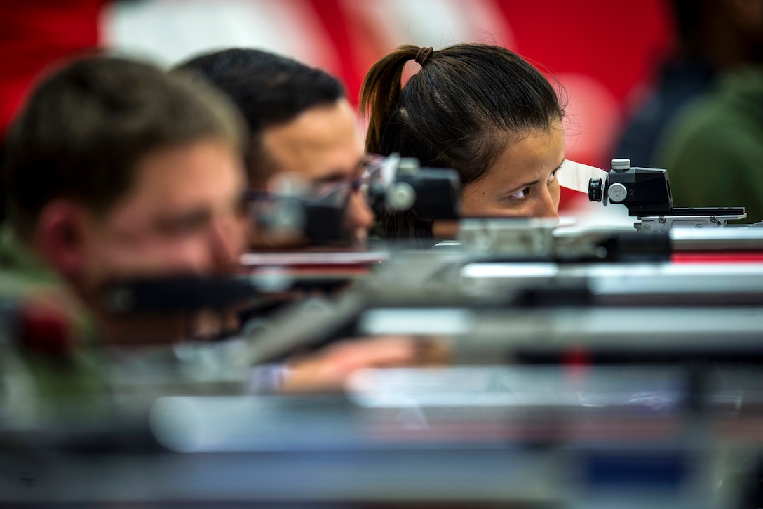 A Marine stares while aiming an air rifle on a firing line with fellow athletes.