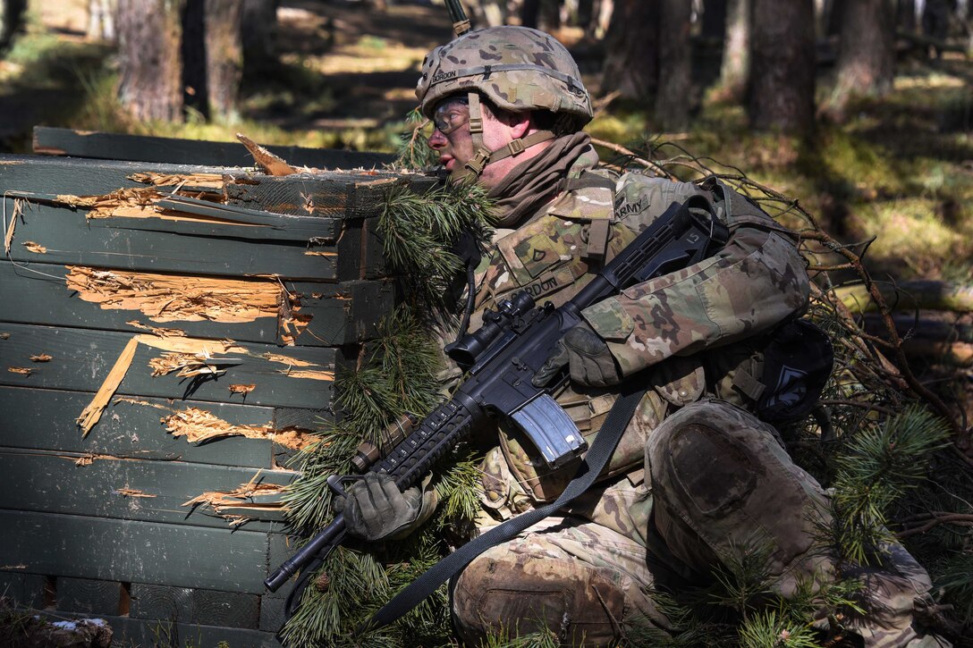 A soldier takes cover behind a wooden obstacle.