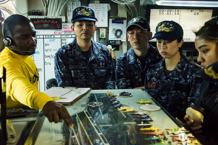 Sailors stand around a display.