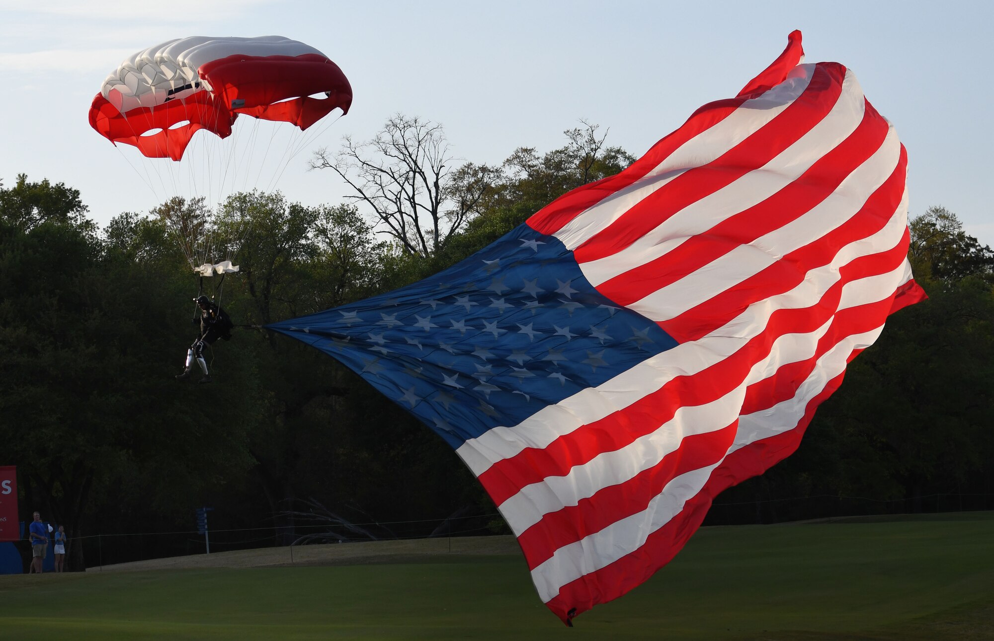 Retired U.S. Army Sgt. 1st Class Dana Bowman, a double amputee, parachutes while carrying the U.S. Flag during the Rapiscan Systems Classic Champions Tour at Fallen Oak Golf Club March 25, 2018, in Saucier, Mississippi. Keesler personnel performed the national anthem and presented the colors during the closing ceremony of the three-day event. This is the fifth year that the event has been held on the coast. (U.S. Air Force photo by Kemberly Groue)