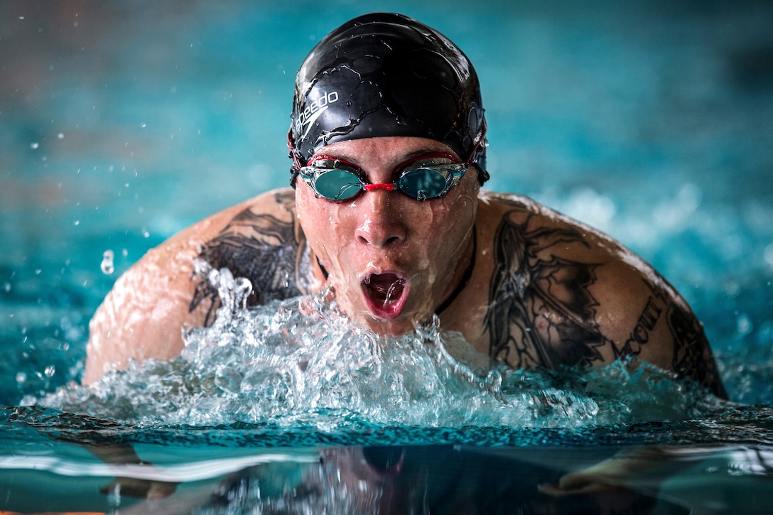 A Marine in a swim cap and goggles takes a deep breath while swimming in a pool.
