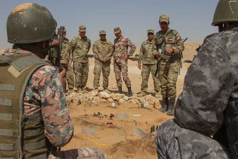 U.S. Soldiers from the 648th Military Engagement Team, Georgia Army National Guard, and instructors from the Jordan Armed Forces Noncommissioned Officer Academy receive a sand-table briefing during the JAF NCOA Squad Leader Course, near Amman, Jordan, March 18, 2018. The 648th MET advised JAF NCOA instructors as the Jordanian leaders developed the program of instruction for the course, which is attended by their soldiers and their regional allies.