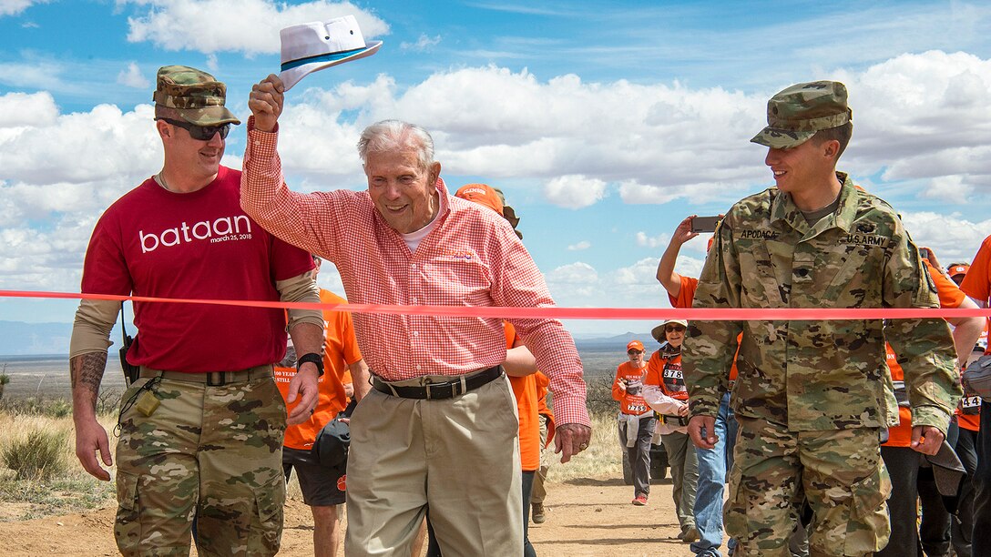 A 100-year-old retired Army colonel and Bataan Death March survivor raises his hat as he crosses the finish line of an event.