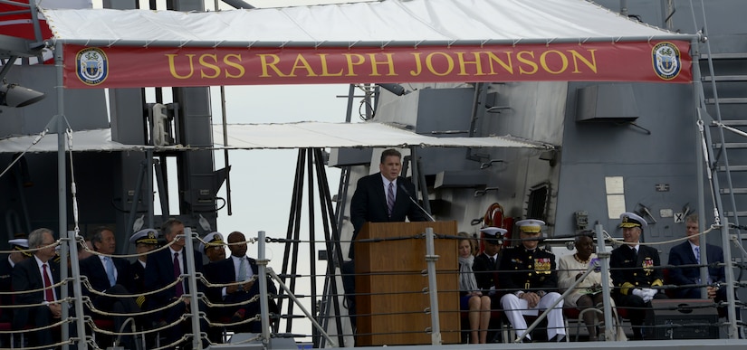 Senior Executive Service Official James Geurts, Assistant Secretary of the Navy for Research, Development & Acquisition, center,  delivers remarks during the USS Ralph Johnson (DDG-114) commissioning ceremony March 24, 2018 at the Port of Charleston, S.C.