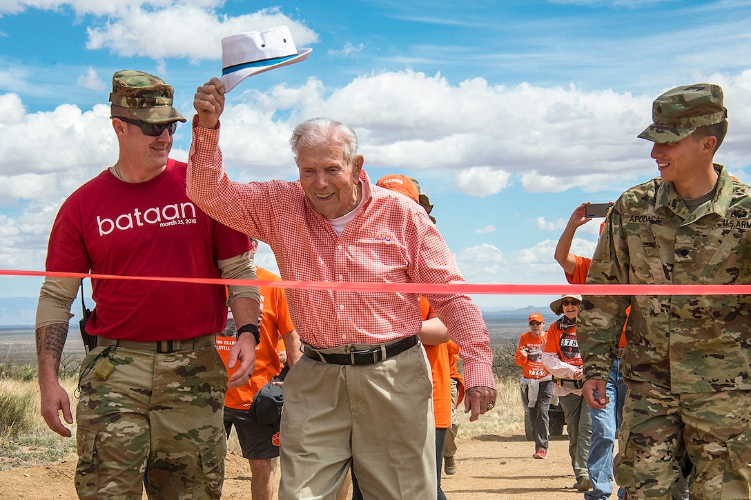 A 100-year-old retired Army colonel and Bataan Death March survivor raises his hat as he crosses the finish line of an event.