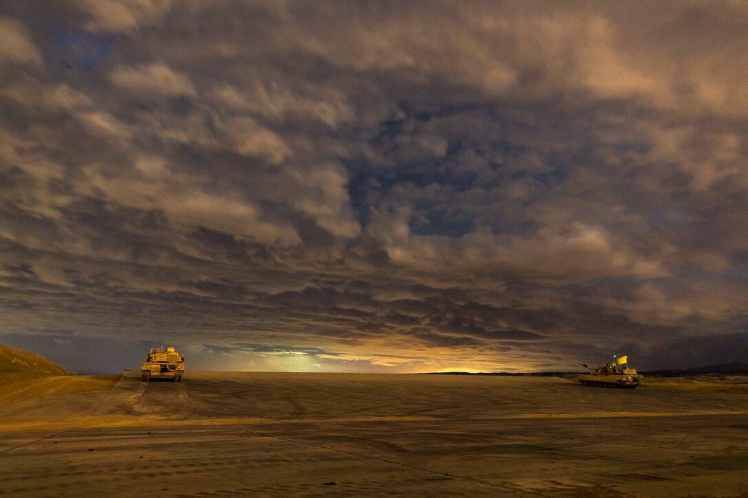 Two tanks sit on a desert-like landscape amid sweeping clouds and fading light.
