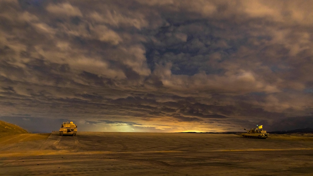 Two tanks sit on a desert-like landscape amid sweeping clouds and fading light.