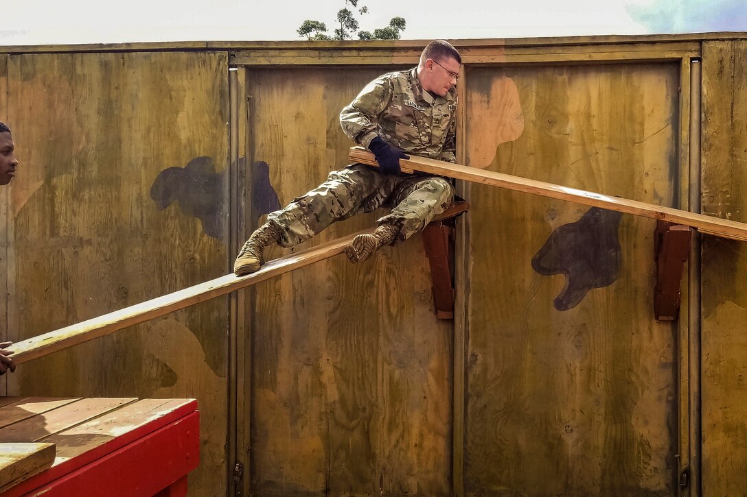 A soldier sits on an elevated wood plank and holds onto another.