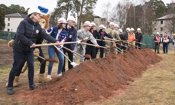 A group of people stand with shovels, tossing dirt.