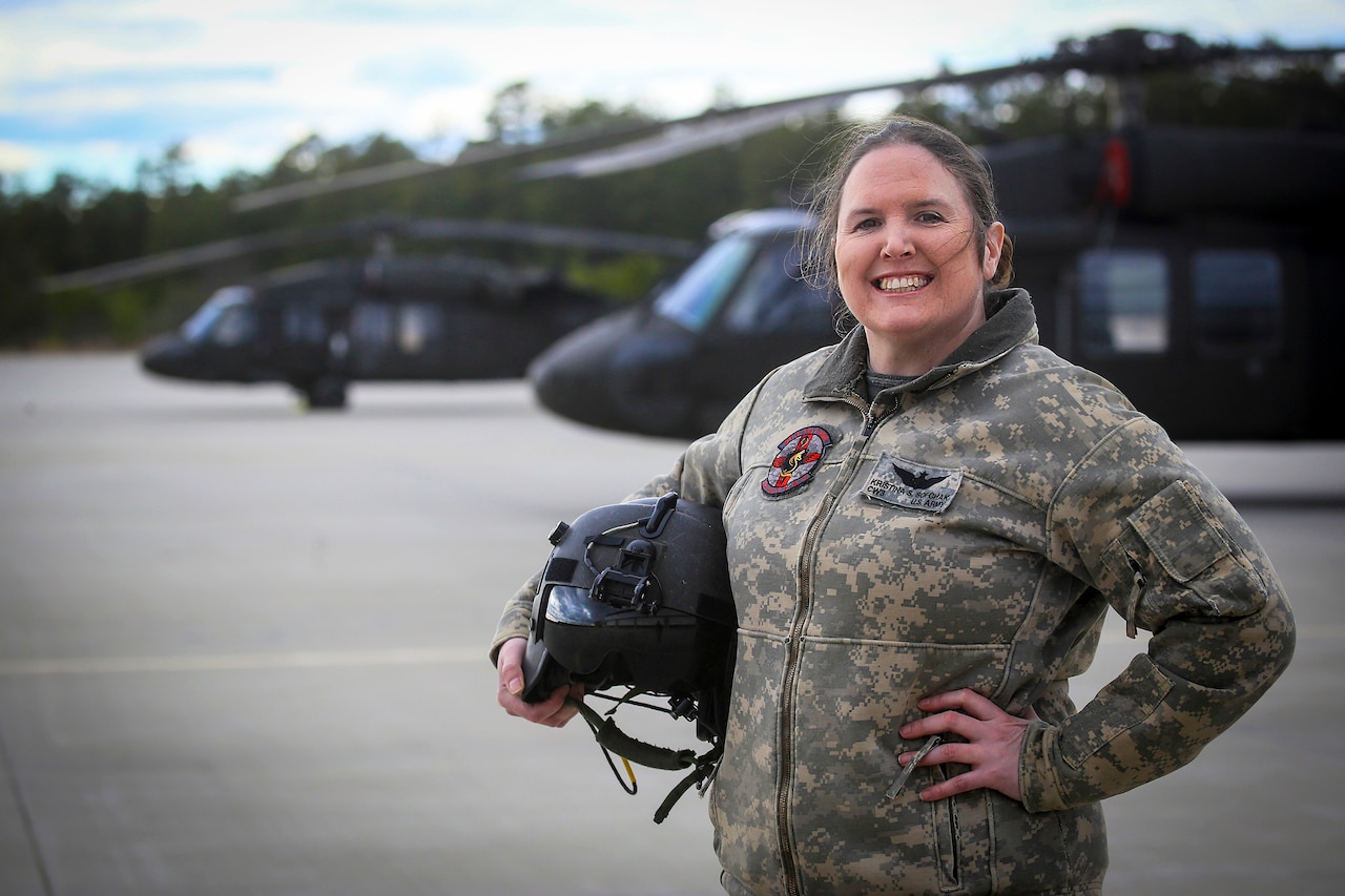 A soldier stands in front of two helicopters.