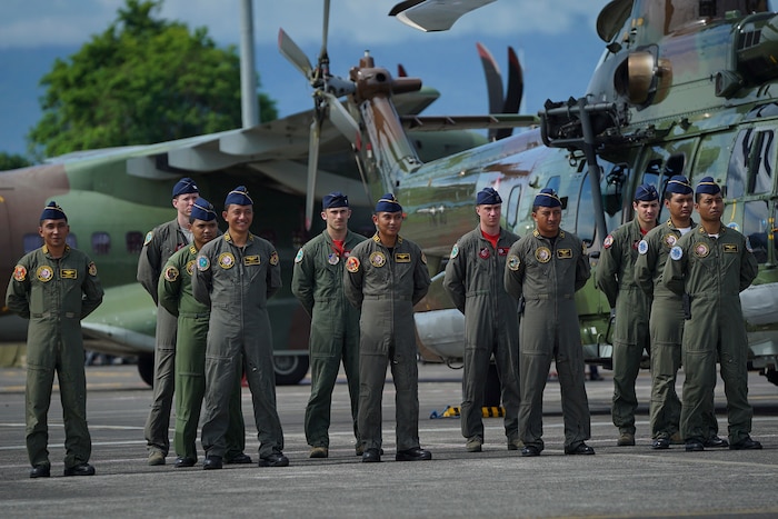 A group airmen pose for a photo in front of a helicopter.