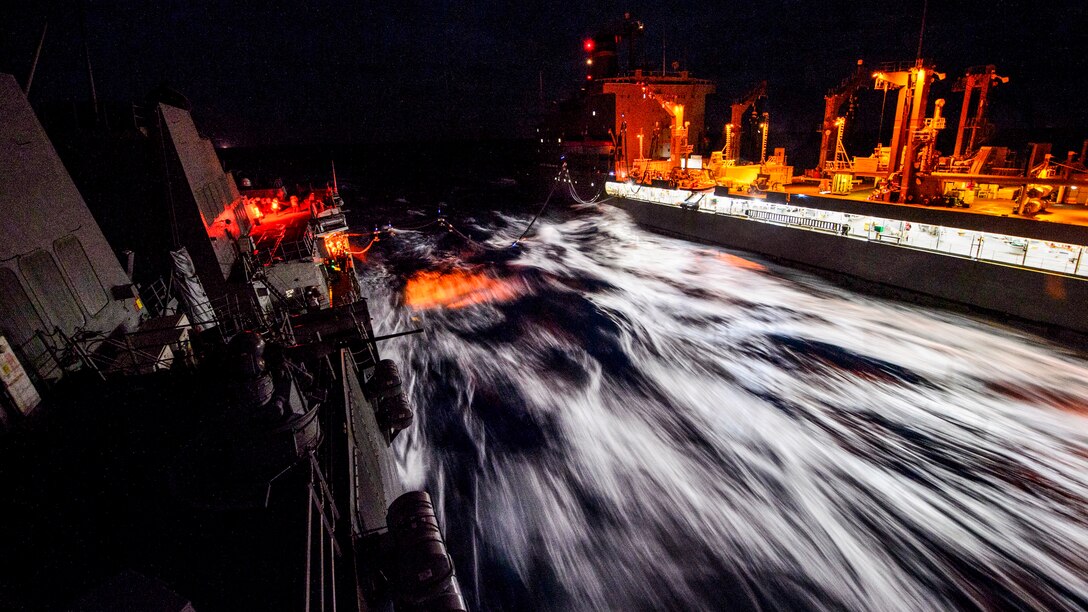 A fleet replenishment oiler sails next to a guided-missile destroyer during a replenishment operation at sea.