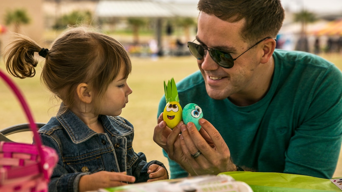 A Marine father holds two decorated eggs during a family day with this daughter.