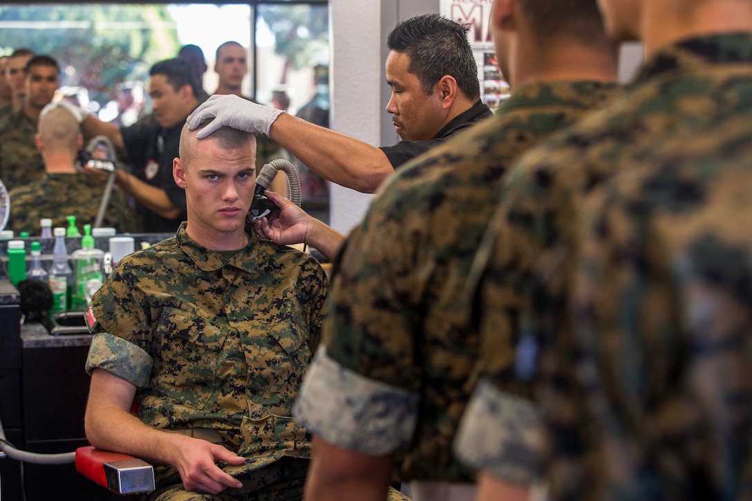A Marine recruit gets a haircut as other recruits stand in line.