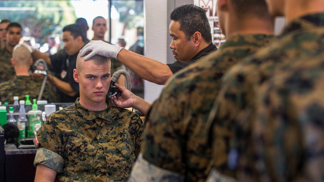 A Marine recruit gets a haircut as other recruits stand in line.