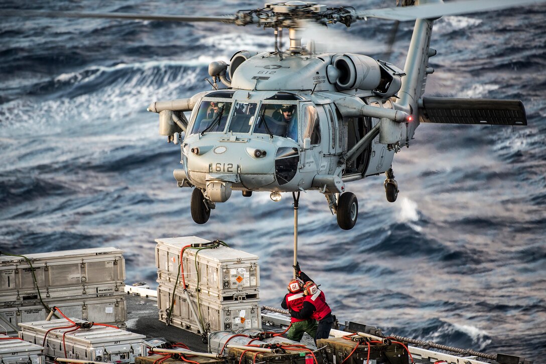 Two sailors help a helicopter offload ammo while at sea.