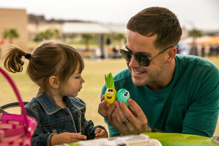 A Marine father holds two decorated eggs during a family day with his daughter.