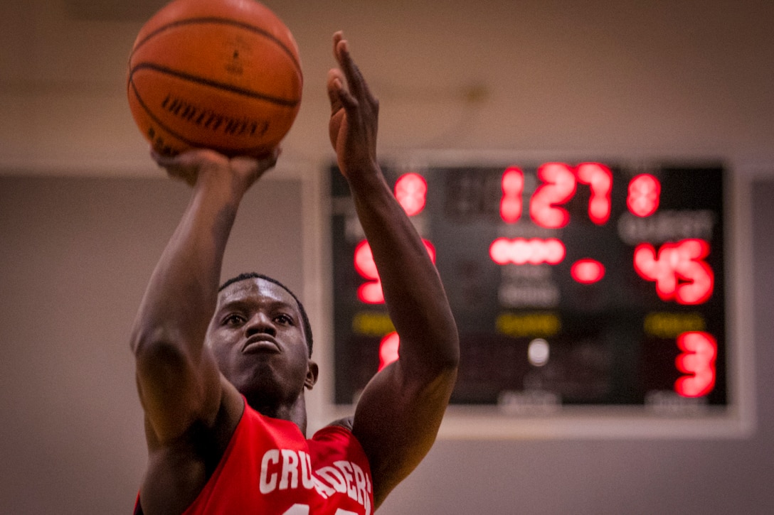 An airman holds a basketball over his head while preparing to take a shot.