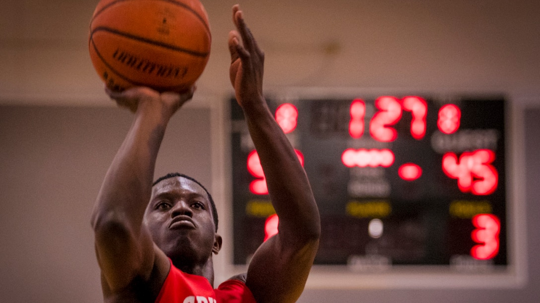 An airman holds a basketball over his head while preparing to take a shot.