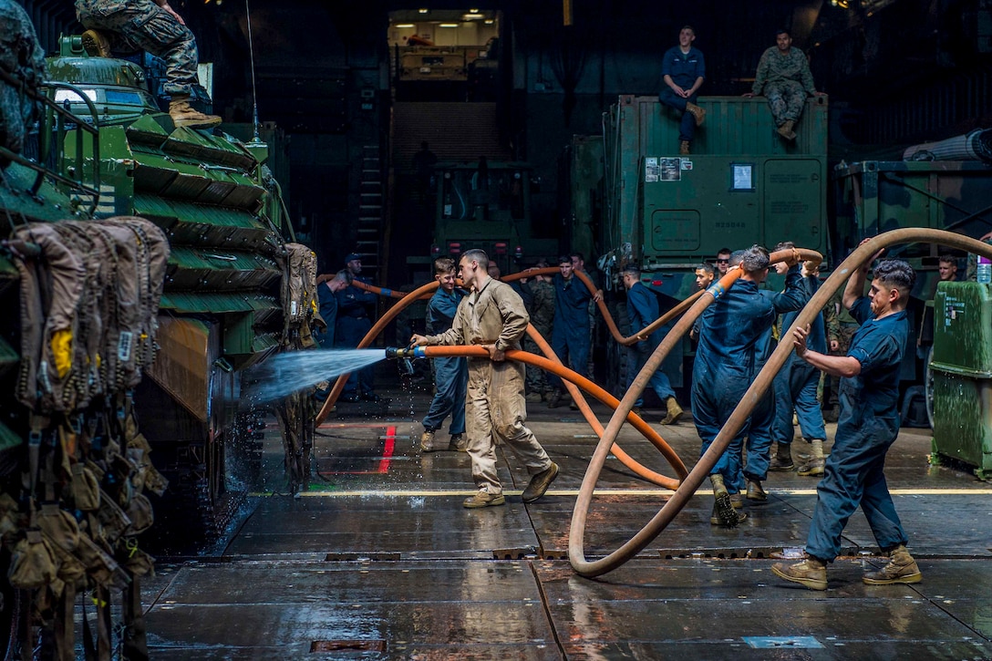 Marines maneuver large hoses in a dark, damp space while washing vehicles.