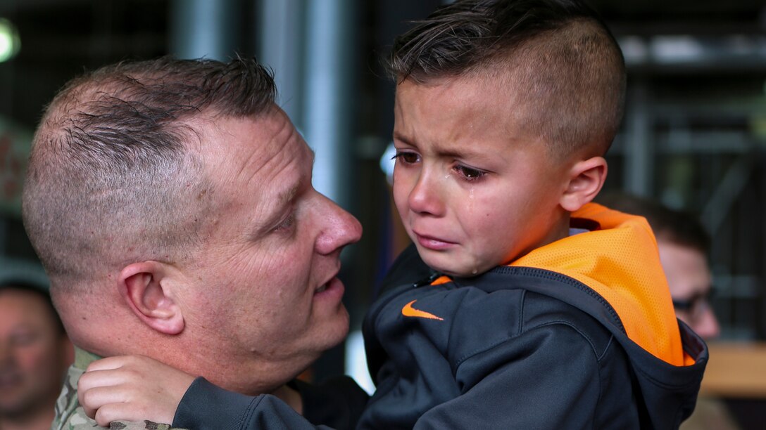 A soldier holds and talks to a crying boy.