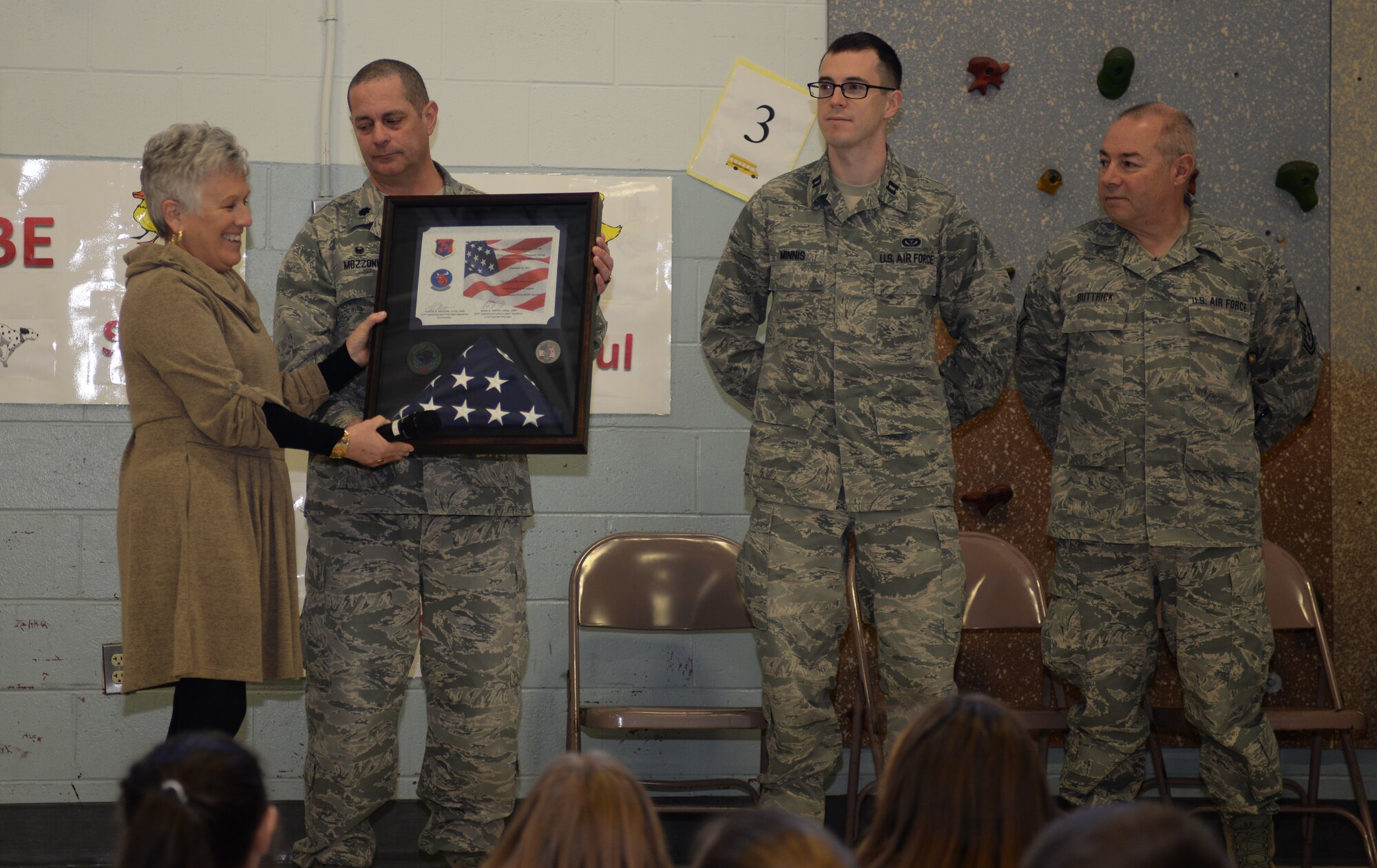 Michelle McAlister, principal for the McClelland Elementary School, accepts a flag and certificate from Lt. Col. Eugene R. Mozzoni, commander of the 157th Civil Engineering Squadron, Captain Erik Minnis and Chief Master Sgt. Todd Buttick, New Hampshire Air National Guard, during a ceremony thanking the students for sending letters to the 157th Civil Engineer Squadron while the unit was deployed to the middle east over the 2017 holiday season, March 27, 2018, Rochester, N.H.  The flag was flown over the country of Kuwait during Christmas while the squadron was deployed there. (N. H. Air National Guard photo by Master Sgt. Thomas Johnson)