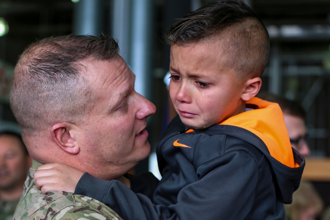 A soldier holds and talks to a crying boy.