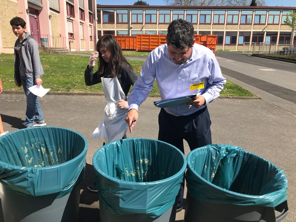 A man with a clip board looks into and points at three trash cans.