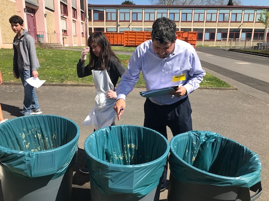 A man with a clip board looks into and points at three trash cans.