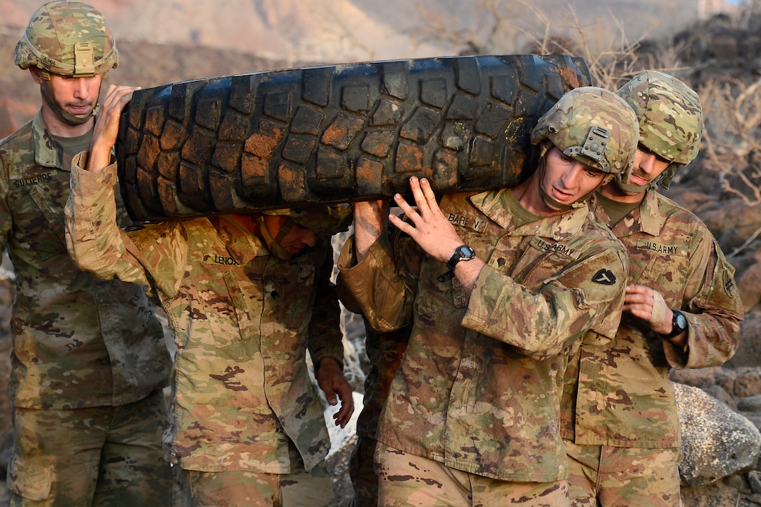 Soldiers carry a tire while navigating an obstacle course.