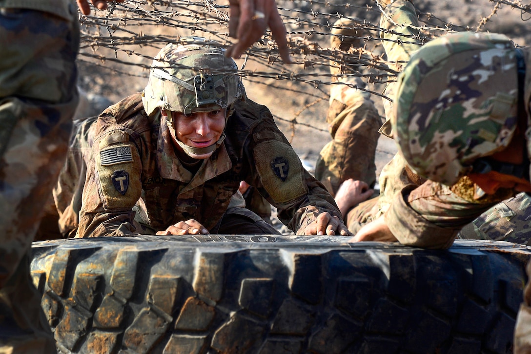 Soldiers push a tire while navigating an obstacle course.