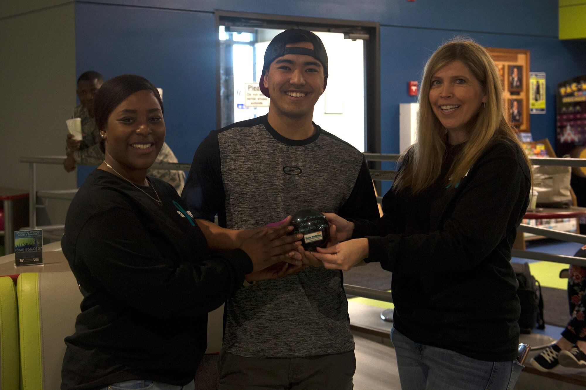 Tech. Sgt. Rayna Anderson, left, 62nd Airlift Wing volunteer victim advocate and sexual assault response team coordinator intern, and Heather Van Mill, right, Sexual Assault Prevention and Response program manager, award Staff Sgt. Tyler Hill, 627th Logistics Readiness Squadron vehicle maintenance journeyman, the prize for top bowling score, April 27, 2018, at Joint base Lewis-McChord, Wash. The event was one of several held during Sexual Assault Awareness and Prevention Month.