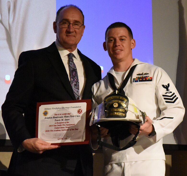 U.S. Fire Administrator, Chief Keith Bryant presents Petty Officer 1st Class Travis Starr, Navy Center for Intelligence and Warfare Training Detachment instructor, with the Tom Smith Fire Equipment instructor of the year award during the Annual Firefighter Ball at the McNease Convention Center, San Angelo, Texas, April 28, 2018. The award is presented to the instructor that has displayed professionalism on the podium, devotion to duty and volunteerism to their unit and the local community. (U.S. Air Force photo by Airman 1st Class Seraiah Hines/Released)