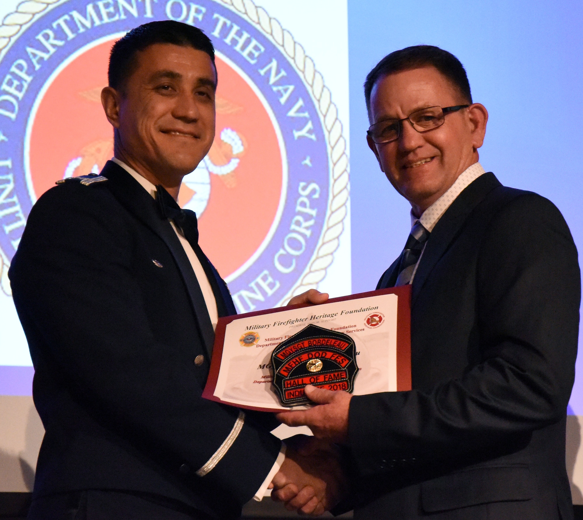 U.S. Air Force Col. Ricky Mills, 17th Training Wing commander, presents retired U.S. Marine Corps Master Gunnery Sgt. Peter Bordeleau, firefighter Hall of Fame inductee, with a new clip to his helmet as congratulations during the 16th Annual Firefighter Ball at the McNease Convention Center, San Angelo, Texas, April 28, 2018. Bordeleau served in the U.S. Marine Corps from 1983-2013, during which he was stationed at Goodfellow on two separate occasions. (U.S. Air Force photo by Airman 1st Class Seraiah Hines/Released)