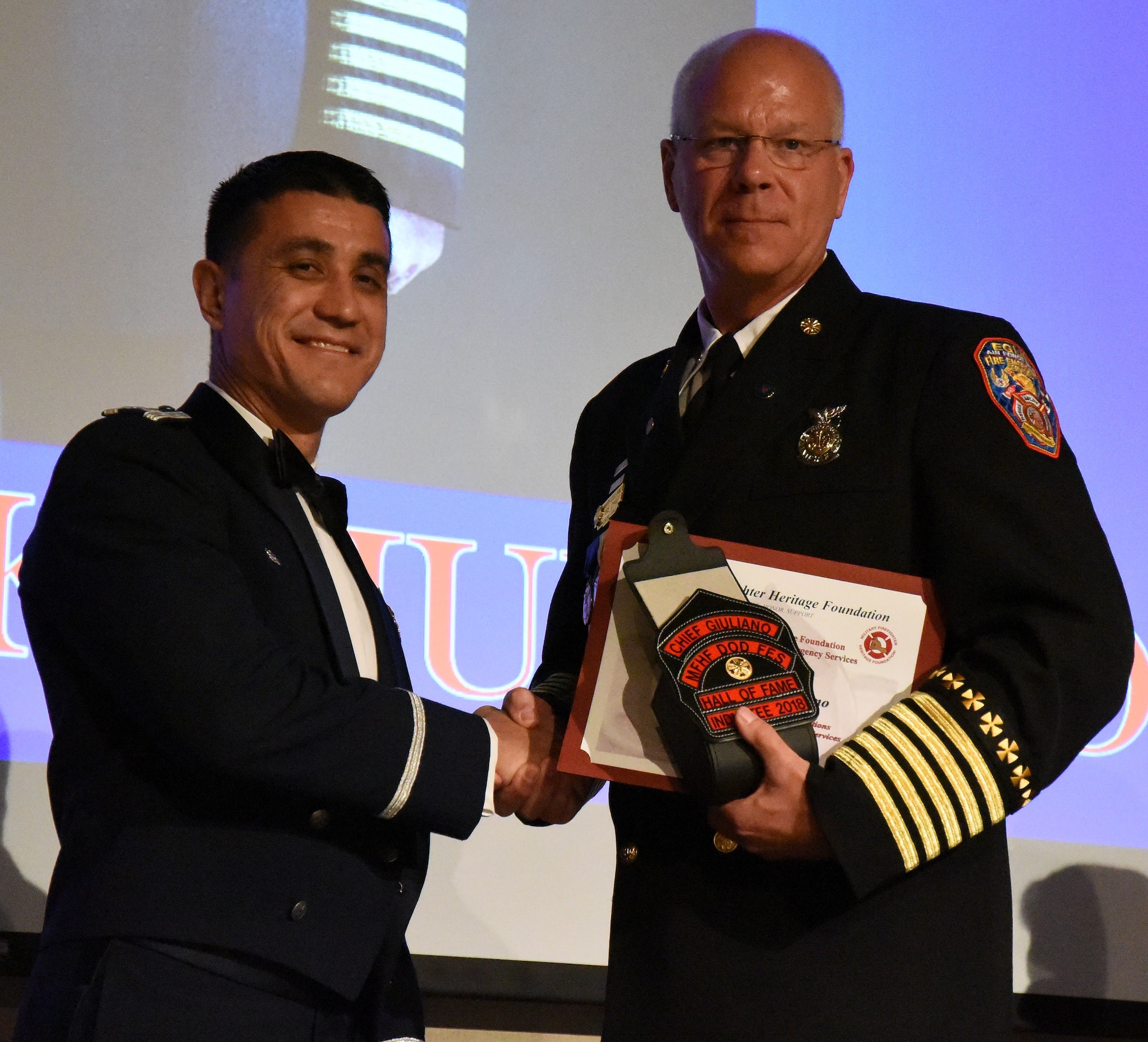 U.S. Air Force Col. Ricky Mills, 17th Training Wing commander, congratulates Chief Mark Guiliano, on receiving the Lifetime Achievement Award and being inducted into the Hall of Fame during the 16th Annual Firefighter Ball at the McNease Convention Center, San Angelo, Texas, April 28, 2018. Guiliano started his career in 1978 as an Air Force firefighter and crossed into the civilian sector in 2001. (U.S. Air Force photo by Airman 1st Class Seraiah Hines/Released)