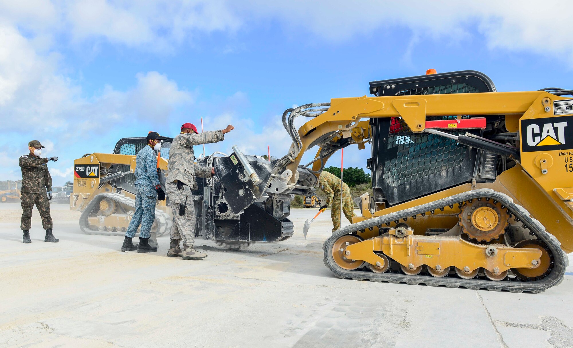 A member of the 554th RED HORSE Squadron, center, guides wingmen of the Republic of Korea Air Force and Republic of Singapore Air Force during the use of a compact track loader saw cutter as part of a training task of exercise Silver Flag April 24, 2018, at Northwest Field, Guam. Teams faced a simulated aftermath of a base attack. They had to repair facilities and the airfield to ensure that they can get the airfield back up and operational. (U.S. Air Force by Airman 1st Class Christopher Quail)