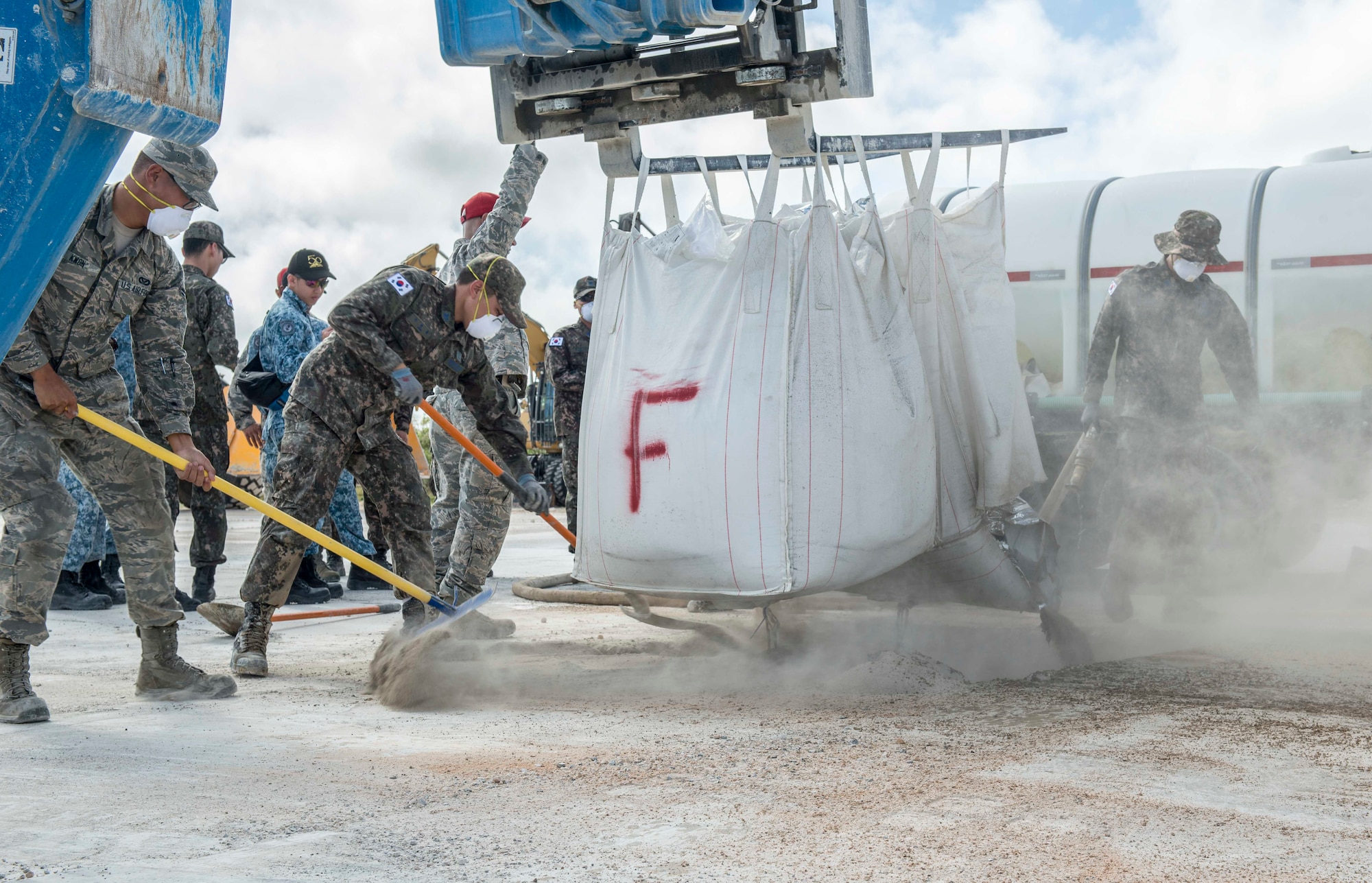 Airmen of the Royal Australian Air Force, Republic of Korea Air Force, Republic of Singapore Air Force and U.S. Air Force fill concrete mix into a hole during exercise Silver Flag, at Northwest Field, Guam, April 24, 2018. Teams faced a simulated aftermath of a base attack and having to repair facilities and the airfield to ensure that they can repair the airfield and return it to safe use for aviators. (U.S. Air Force by Airman 1st Class Christopher Quail)