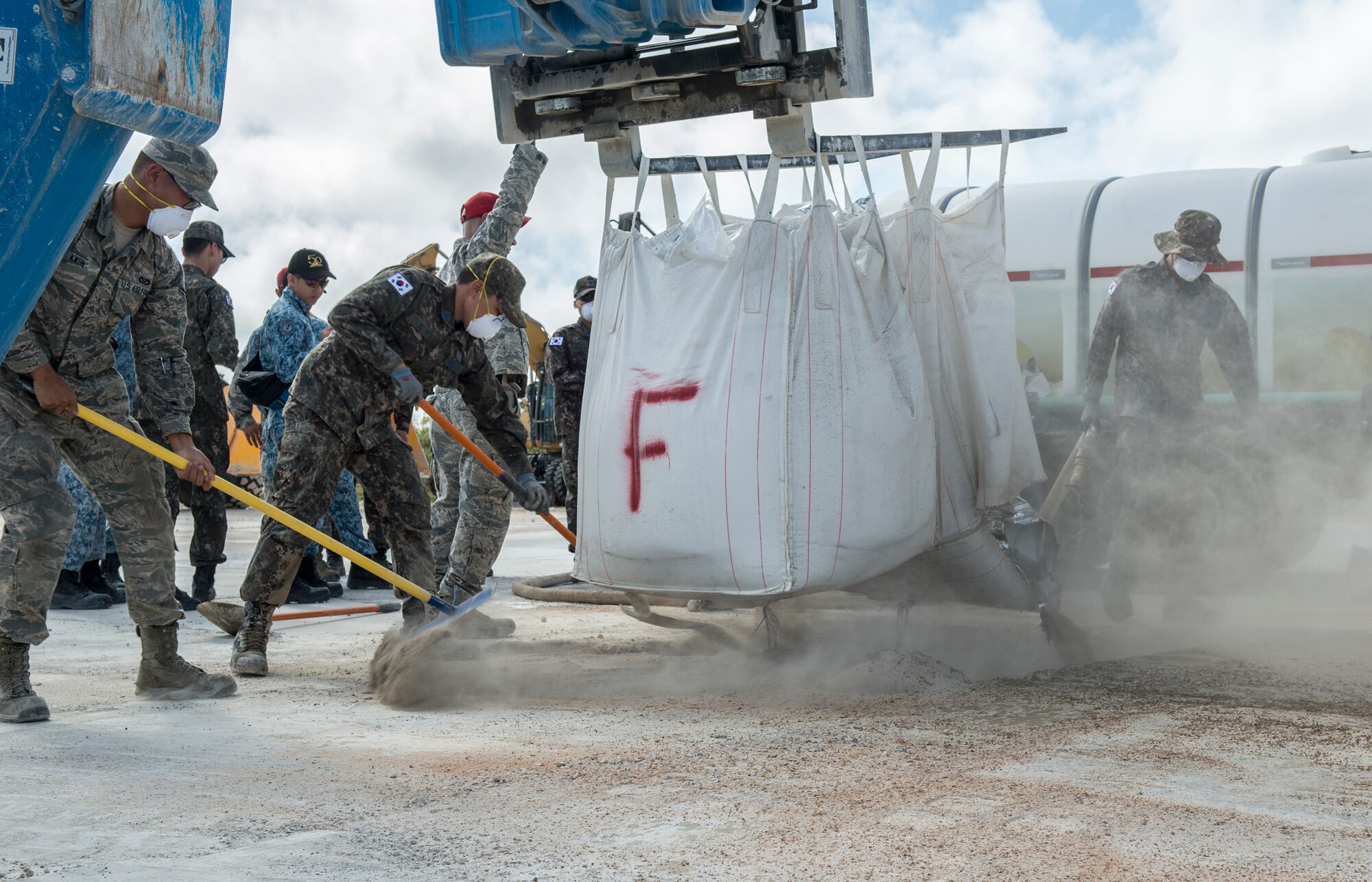 U.S. Air Force Airmen, Royal Australian Air Force, Republic of Korea Air Force, and Republic of Singapore Air Force fillconcrete mix into a hole during Silver Flag April 24, 2018, at Northwest Field, Guam. Teams faced a simulated aftermath of a base attack and having to repair facilities and the airfield to ensure that they can get the airfield back up and operational. (U.S. Air Force by Airman 1st Class Christopher Quail)
