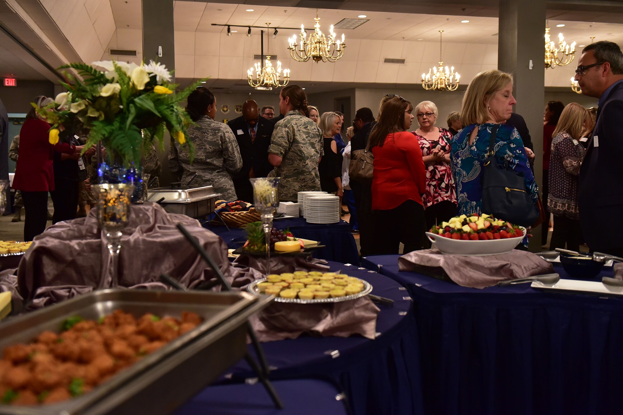 Multiple people talk to each other with a table of food in the foreground.