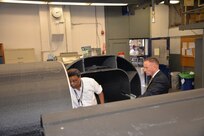 Deputy Assistant Secretary of the Navy for Unmanned Systems Frank Kelley (right) listens to Garry Shields, director of the Disruptive Technologies Lab, on April 20, 2018, as Shields explains the second version of the Optionally Manned Technology Demonstrator that is being readied for hydrodynamic testing at Naval Surface Warfare Center, Carderock Division in West Bethesda, Md. (U.S. Navy photo by Kelley Stirling/Released)
