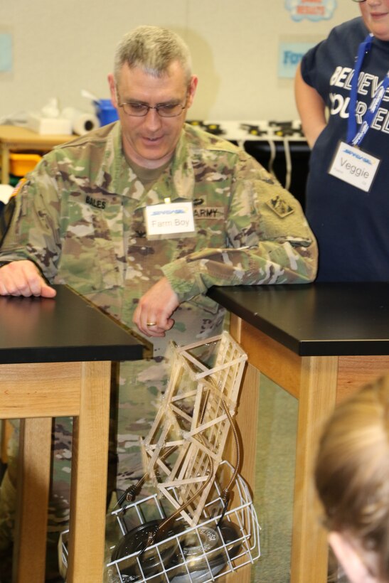 Col. Stephen Bales, U.S. Army Corps of Engineers' Middle East District commander, tests teams' bridges for amount of weight each could hold before failing. This team's bridge held 21 pounds during the bridge building phase of his STARBASE Academy presentation on engineering.