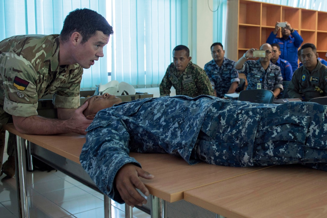 Navy Petty Officer 2nd Class Ros Vudy and Royal Army Cpl. Darren Phillips demonstrate spine immobilization techniques during a basic first responder course.
