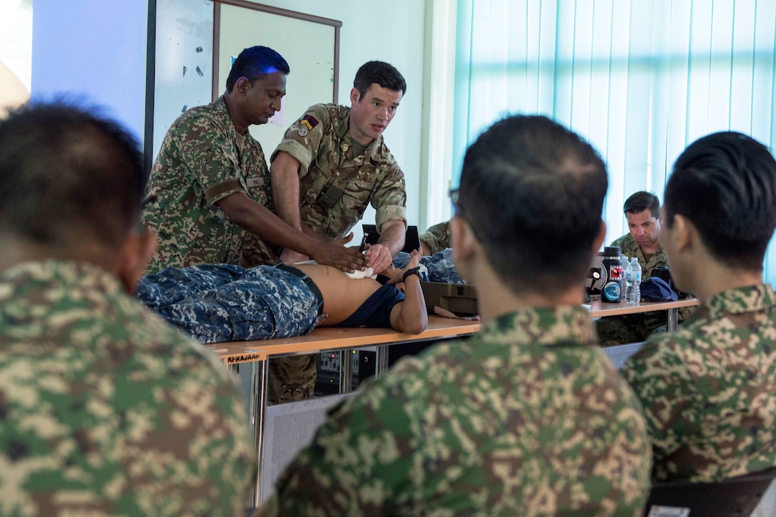 A Navy seaman and Royal Army soldier demonstrate bandaging techniques.