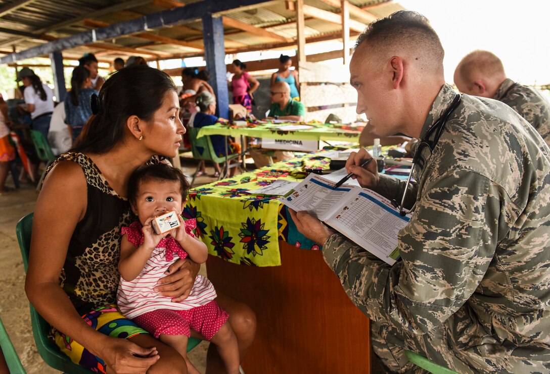 U.S. Air Force Capt. Charles Hutchings, 346th Expeditionary Medical Operations Squadron pediatrician, explains info to a local woman near.