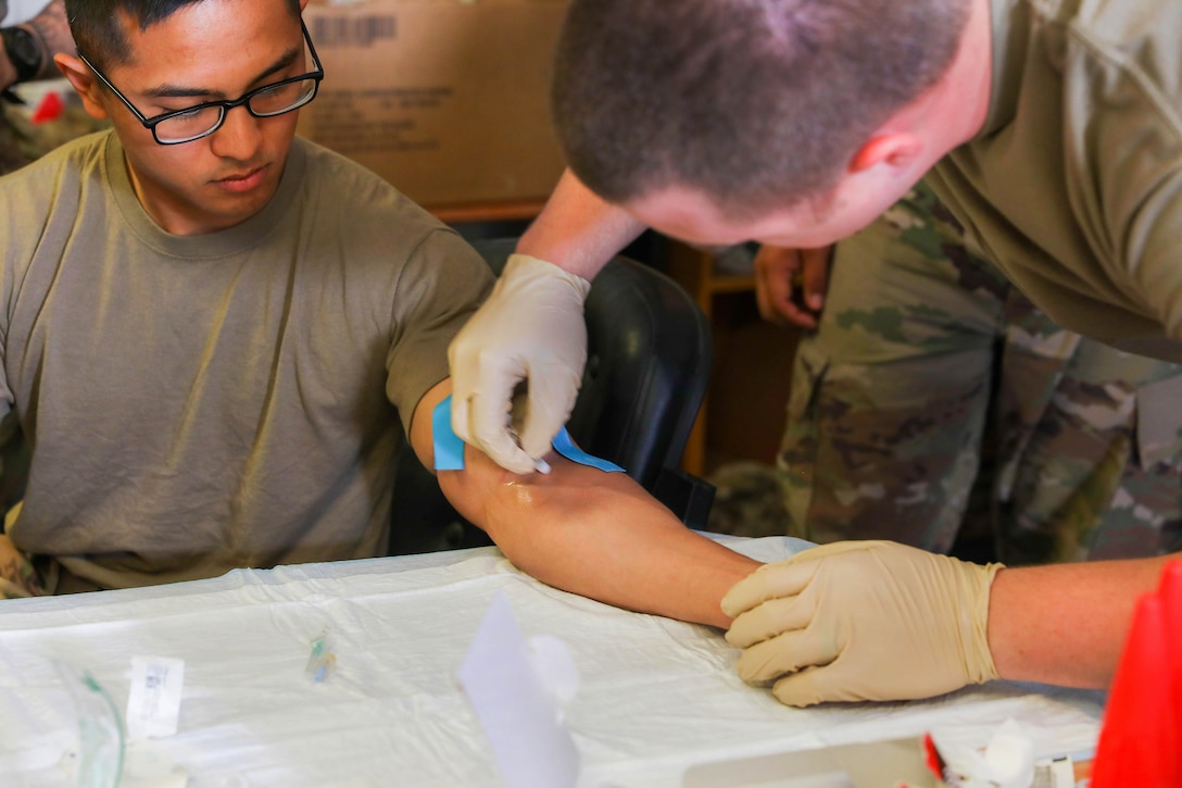 A soldier demonstrates how to sanitize a comrade’s arm.