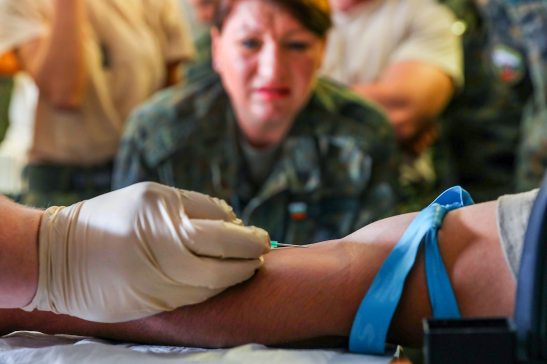 A soldier demonstrates how to insert a needle into the arm of a patient.
