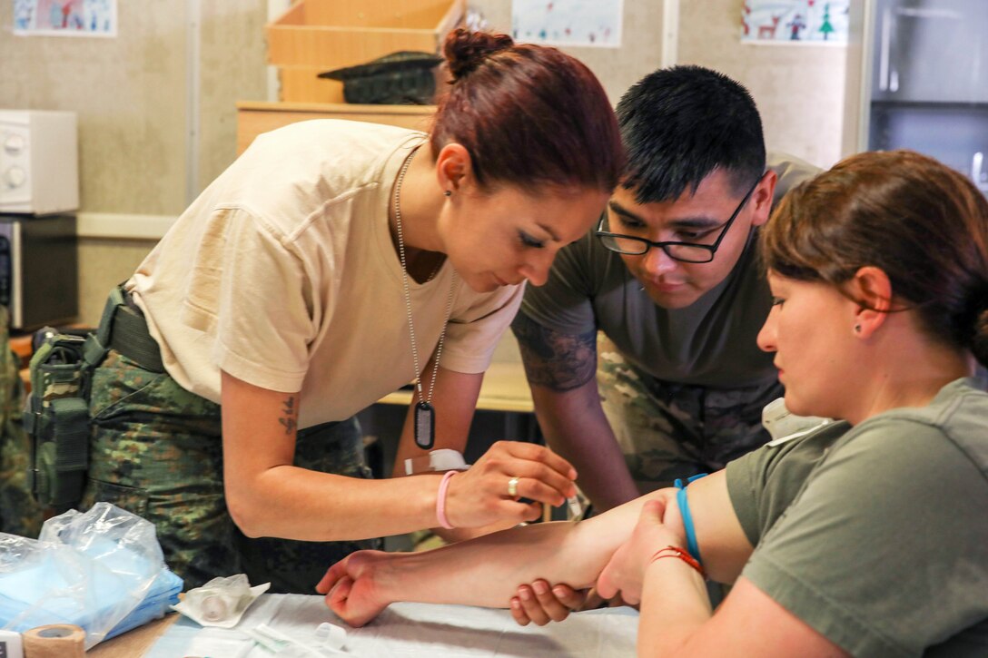 A U.S. soldier watches as a Bulgarian army medical soldier sanitizes her peer’s arm.