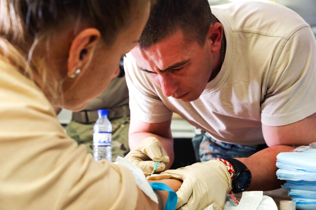 A Bulgarian army medical soldier inserts a hypodermic needle into his peer’s arm.
