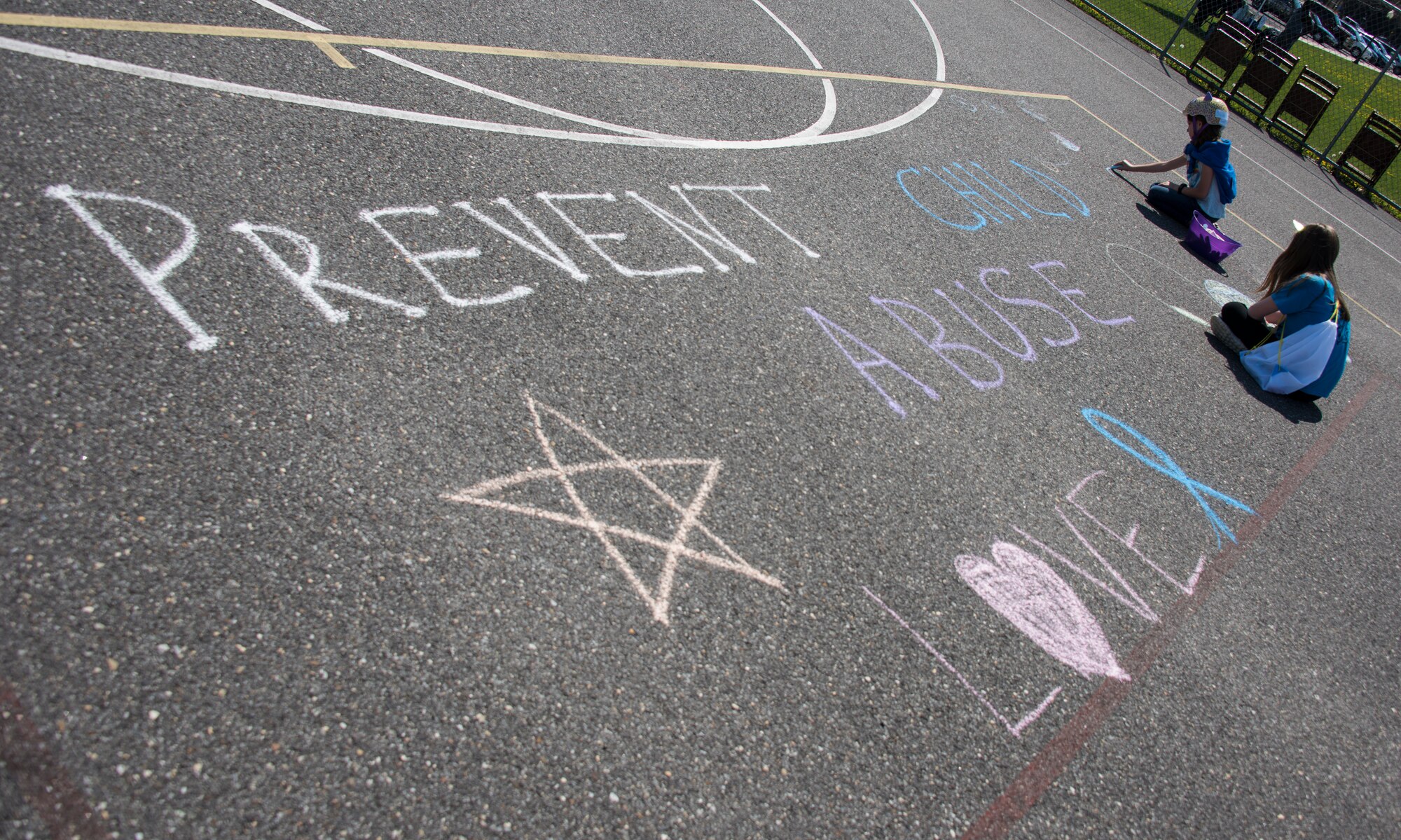 Children draw with chalk on a basketball court during the Kids on Wheels Parade on Joint Base McGuire-Dix-Lakehurst, N.J., April 28, 2018. Children from the Joint Base MDL community drew around the words “Prevent Child Abuse” during the parade. (U.S. Air Force photo by Airman Ariel Owings)